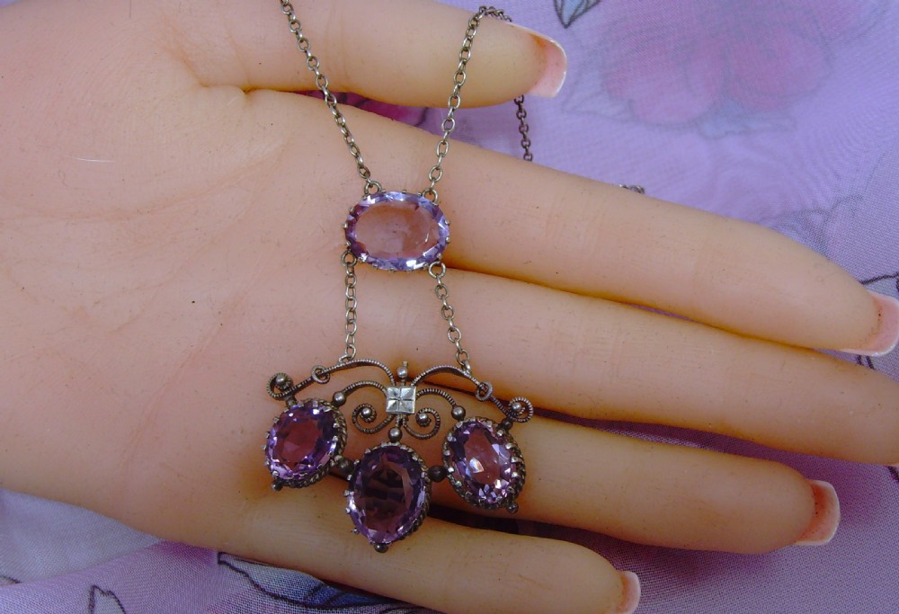 An Arts and Crafts era silver necklace featuring four faceted oval purple amethyst gemstones set within a scrollwork pendant suspended from a fine link chain. View V