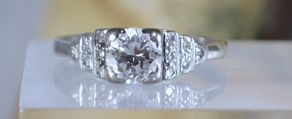 An Art Deco platinum and gold ring featuring a central round diamond set in a square frame with tiered, milgrain-detailed shoulders. View III