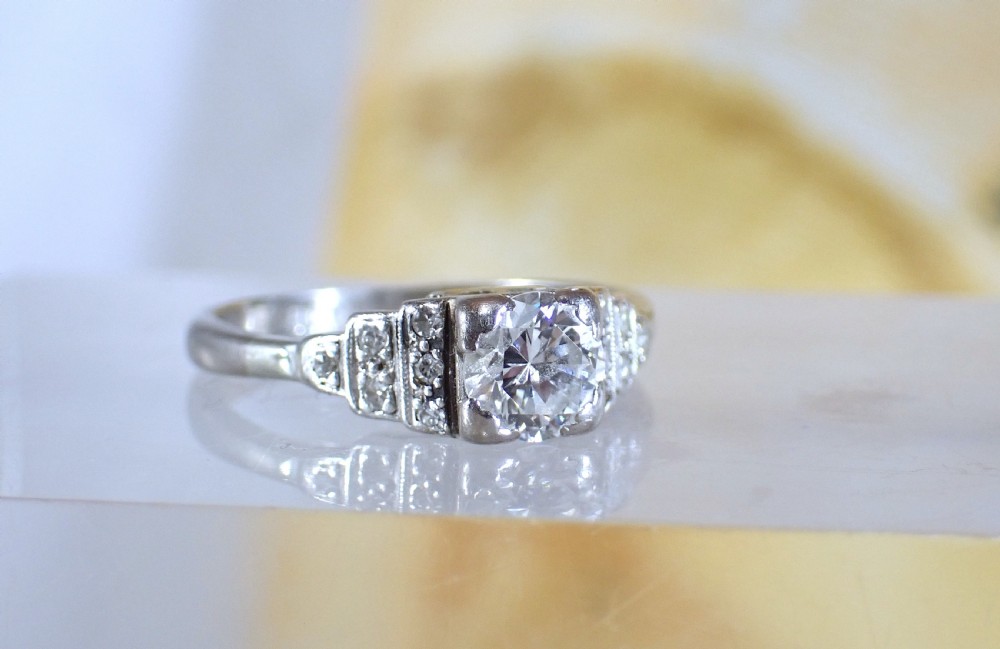 An Art Deco platinum and gold ring featuring a central round diamond set in a square frame with tiered, milgrain-detailed shoulders. View IV