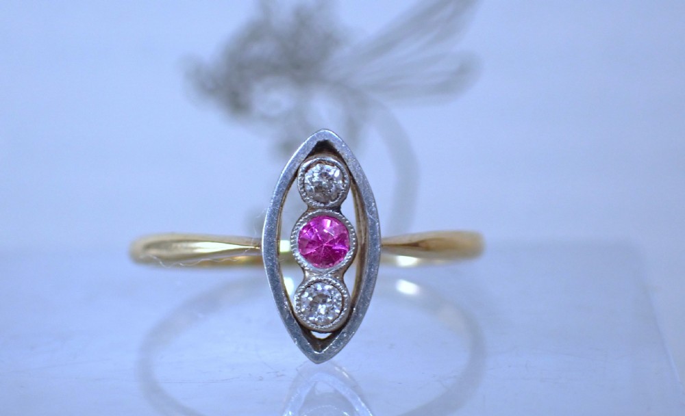 An Art Deco 18ct yellow gold and platinum ring featuring a vertical marquise bezel setting with a central round ruby flanked by two diamonds.