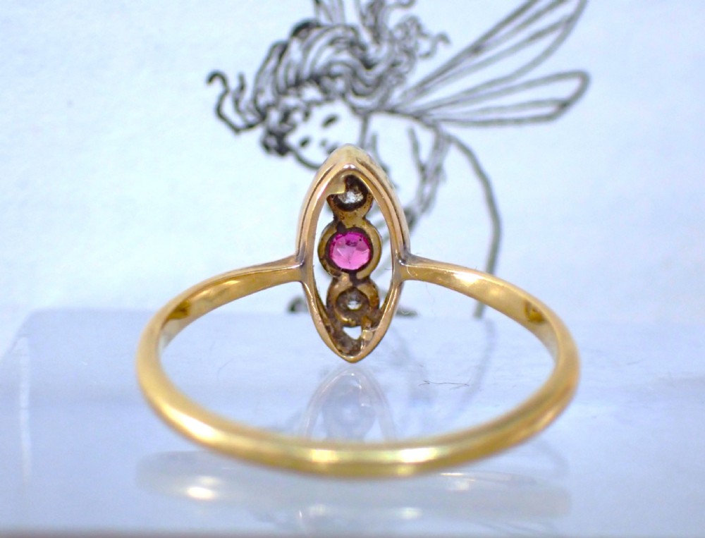 An Art Deco 18ct yellow gold and platinum ring featuring a vertical marquise bezel setting with a central round ruby flanked by two diamonds. View VI