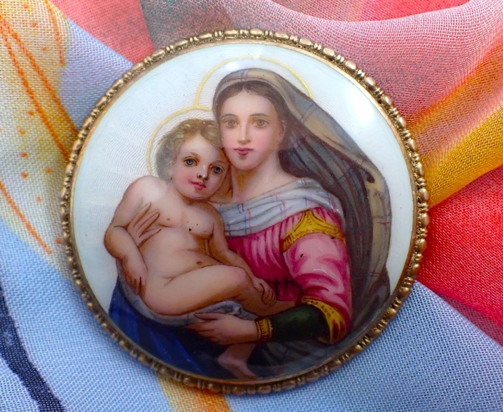 A circular Edwardian silver brooch featuring a hand-painted enamel depiction of the Madonna holding the Christ child within a beaded metal rim.