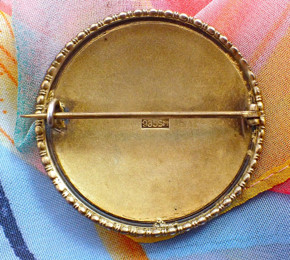 A circular Edwardian silver brooch featuring a hand-painted enamel depiction of the Madonna holding the Christ child within a beaded metal rim. View IV