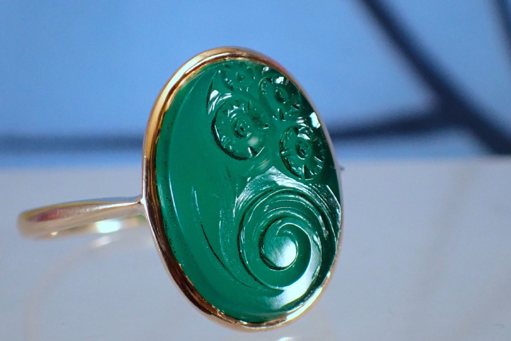 An Art Deco gold ring set with an oval green chalcedony gemstone featuring low-relief floral and scroll carving.
