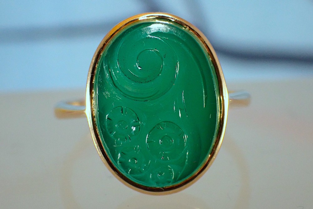 An Art Deco gold ring set with an oval green chalcedony gemstone featuring low-relief floral and scroll carving. View II