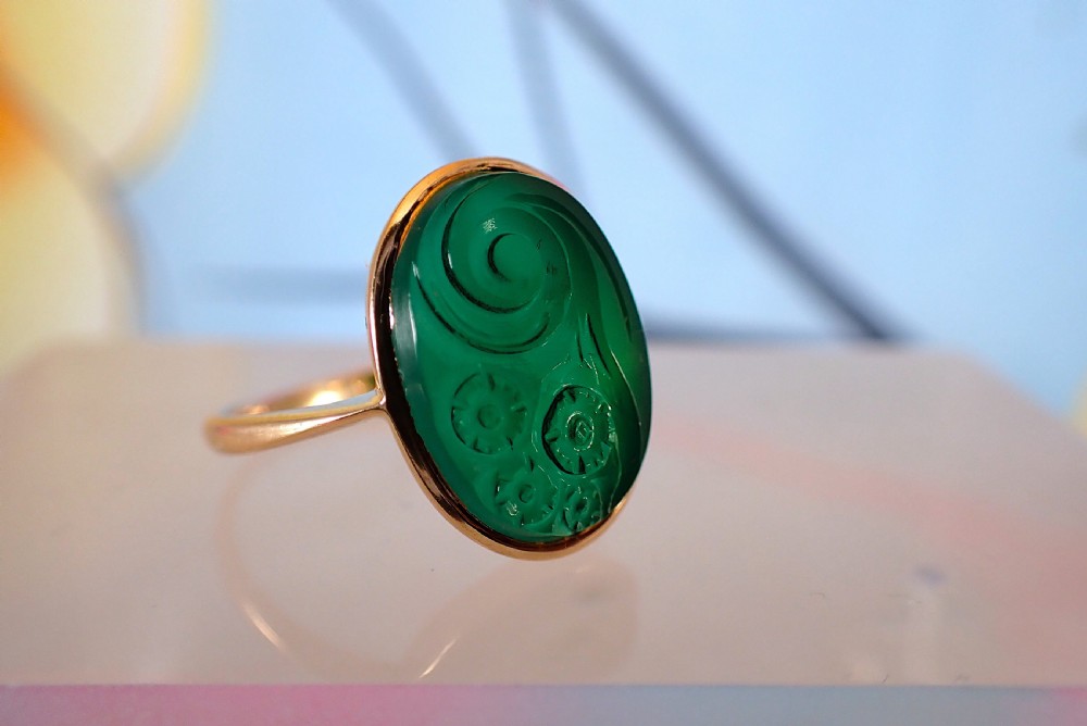An Art Deco gold ring set with an oval green chalcedony gemstone featuring low-relief floral and scroll carving. View V