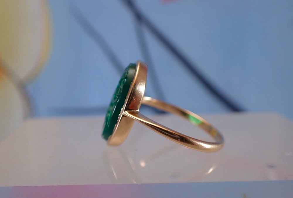 An Art Deco gold ring set with an oval green chalcedony gemstone featuring low-relief floral and scroll carving. View VI