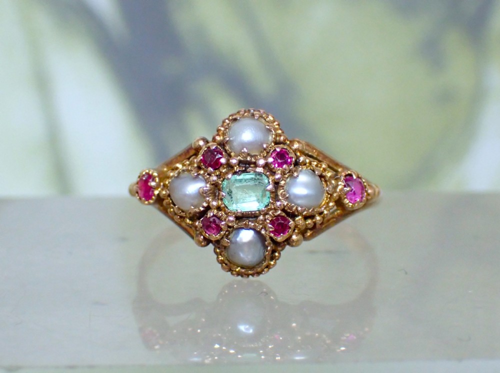 A Georgian 15ct gold ring featuring a central emerald framed by rubies and pearls in a cluster setting on a split-shank band.