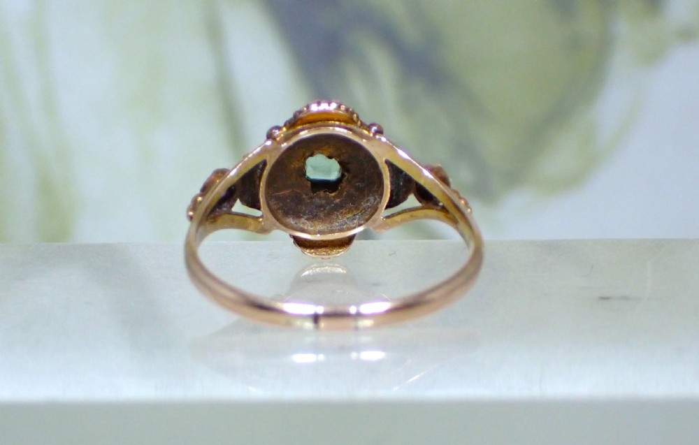 A Georgian 15ct gold ring featuring a central emerald framed by rubies and pearls in a cluster setting on a split-shank band. View VI