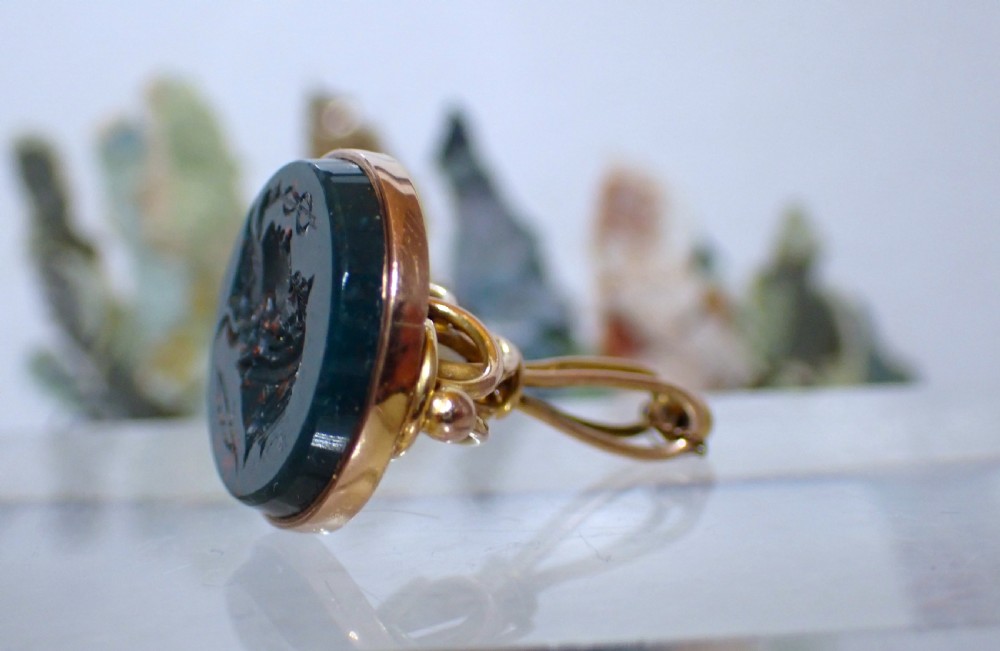 A 9ct yellow gold antique fob seal featuring a carved dark green bloodstone intaglio set in a bezel mount with a looped top.