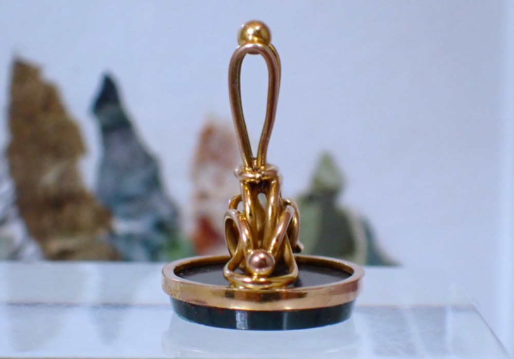 A 9ct yellow gold antique fob seal featuring a carved dark green bloodstone intaglio set in a bezel mount with a looped top. View V