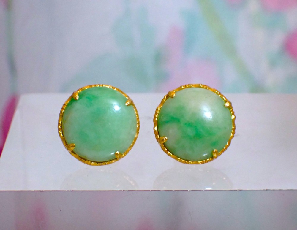 A pair of round green jade cabochon stud earrings held in textured 18ct gold claw settings.