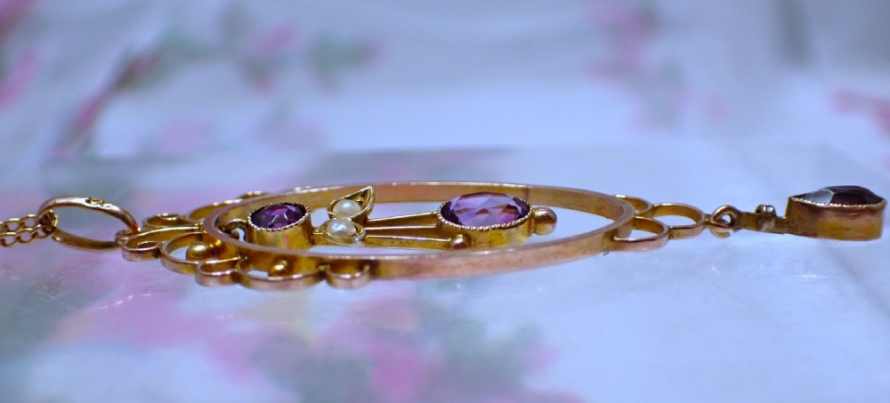An Art Nouveau 9ct gold openwork oval pendant set with three purple amethysts and seed pearls suspended on a gold chain. View IV