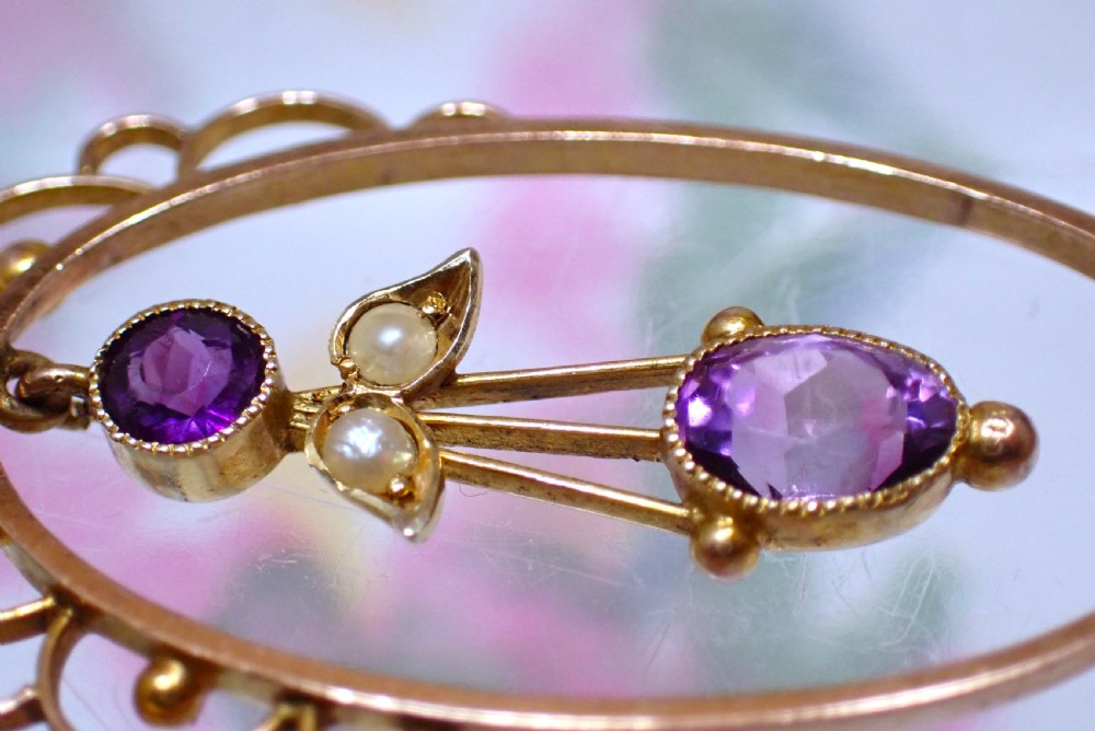 An Art Nouveau 9ct gold openwork oval pendant set with three purple amethysts and seed pearls suspended on a gold chain. View V