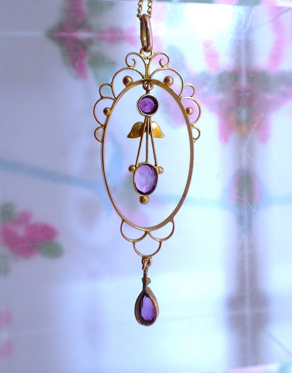 An Art Nouveau 9ct gold openwork oval pendant set with three purple amethysts and seed pearls suspended on a gold chain. View VII