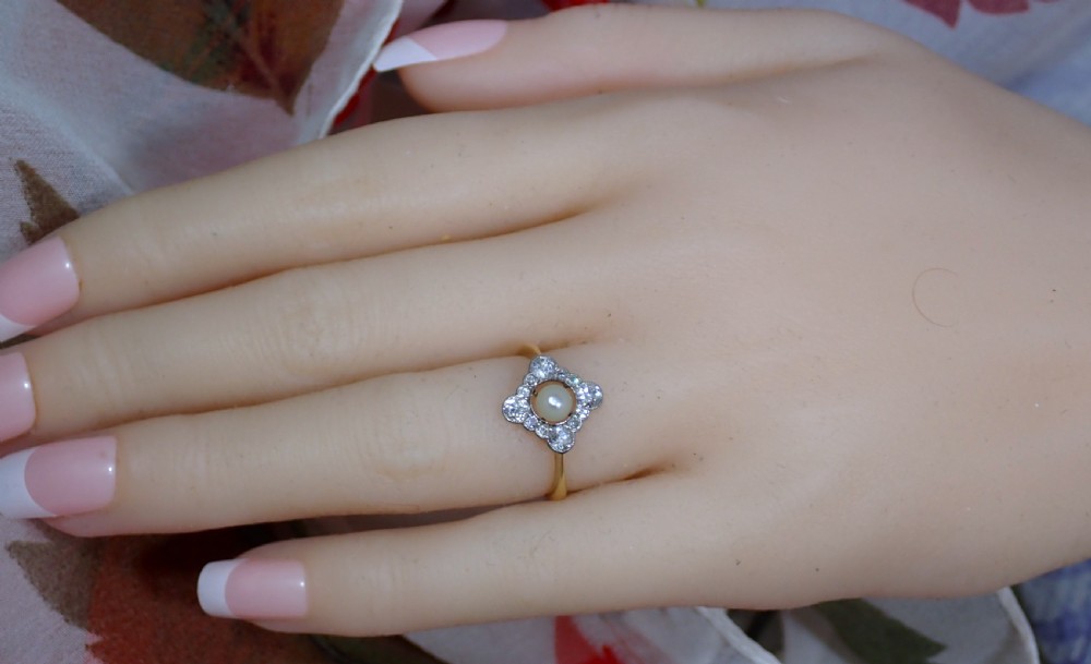 An antique Edwardian ring featuring a central natural pearl surrounded by a pierced diamond-set lozenge frame on an 18ct gold band. View V