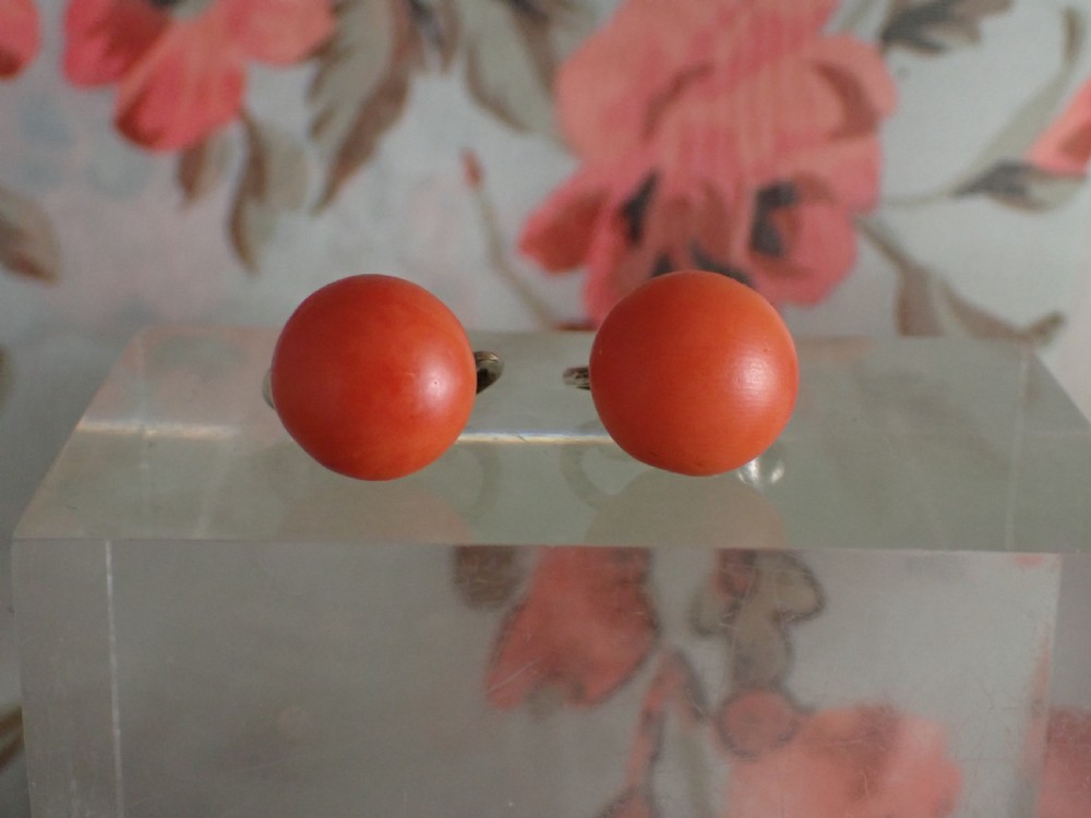 A pair of round, polished orange coral stud-style clip-on earrings mounted on silver backings.