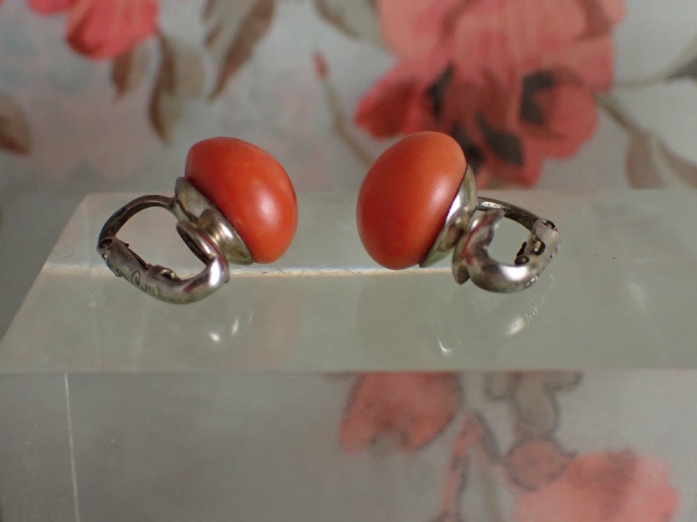A pair of round, polished orange coral stud-style clip-on earrings mounted on silver backings. View III