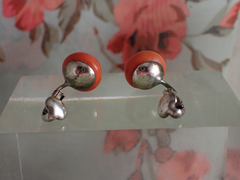 A pair of round, polished orange coral stud-style clip-on earrings mounted on silver backings. View IV