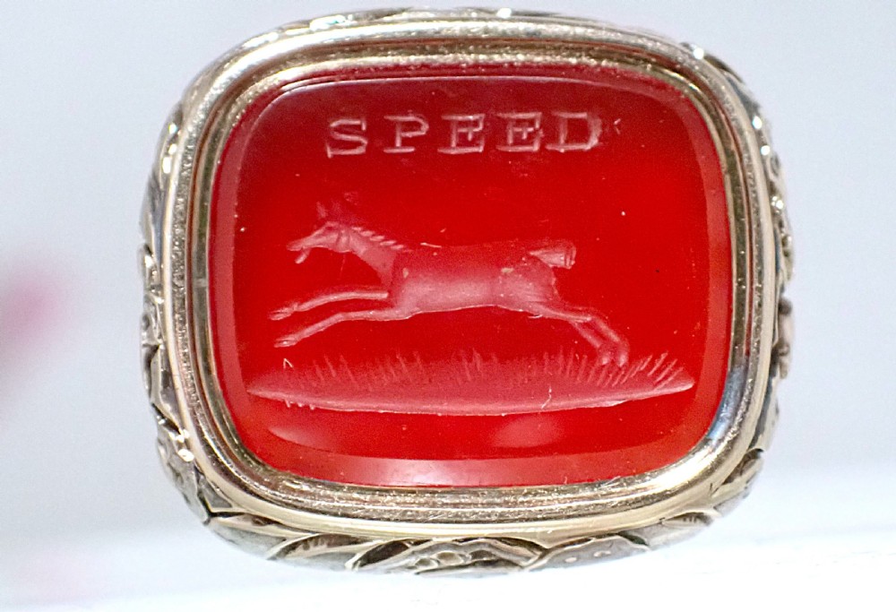 A Georgian gold cased fob seal featuring a carved red carnelian intaglio depicting a galloping horse under the engraved word SPEED.