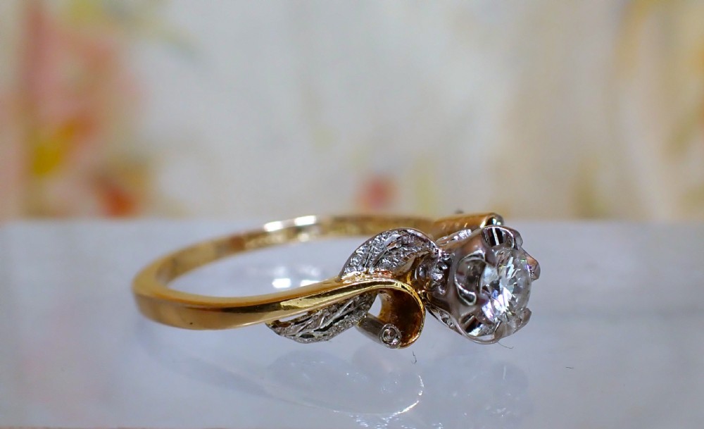 A vintage 18ct yellow gold solitaire ring featuring a central round brilliant-cut diamond set in an illusion mount with carved leaf shoulders. View II