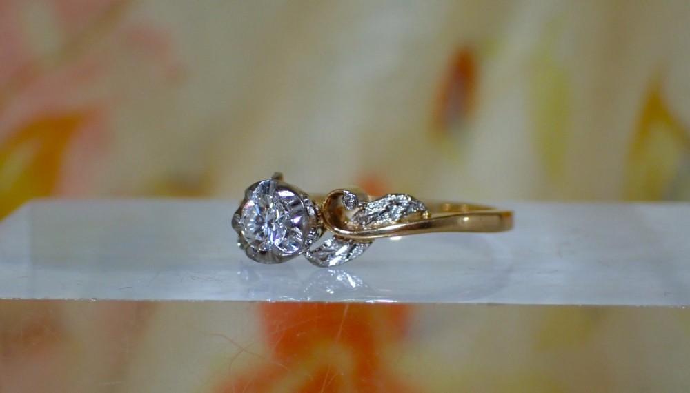 A vintage 18ct yellow gold solitaire ring featuring a central round brilliant-cut diamond set in an illusion mount with carved leaf shoulders. View III