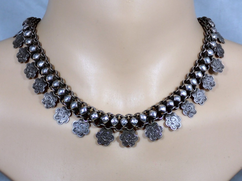 A Victorian silver collar necklace featuring woven link chain strands embellished with faceted beads and dangling engraved floral charms.