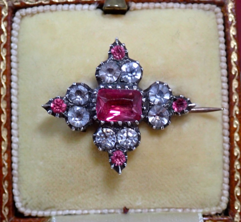 A cruciform Georgian brooch set with silver-topped black dot paste stones around a central rectangular pink ruby-coloured paste gem.