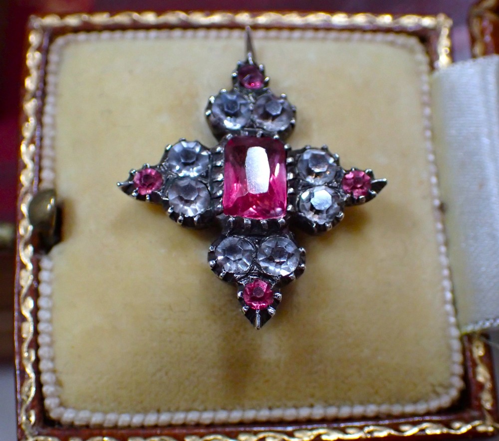 A cruciform Georgian brooch set with silver-topped black dot paste stones around a central rectangular pink ruby-coloured paste gem. View II