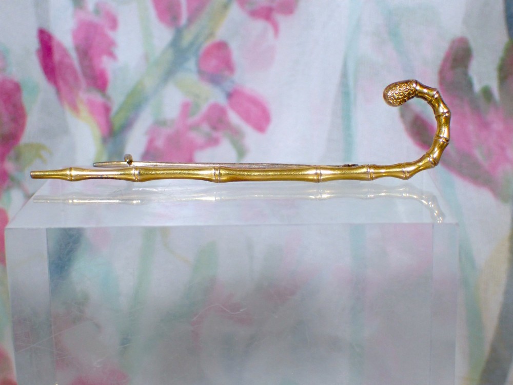 An Edwardian 15ct yellow gold brooch rendered in the shape of a bamboo walking cane with a textured crook handle.