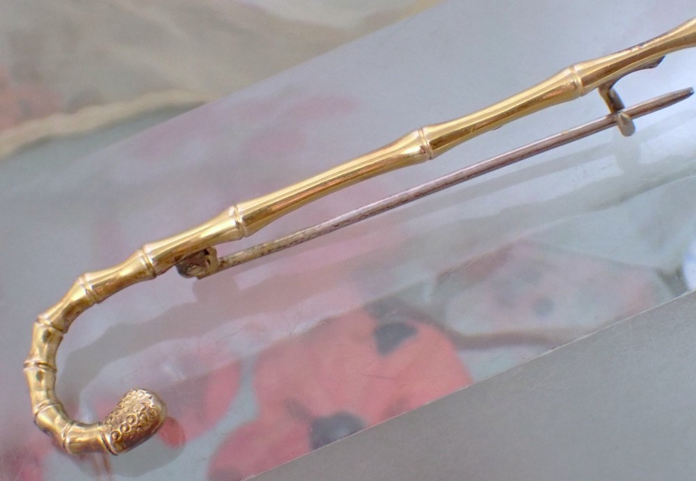 An Edwardian 15ct yellow gold brooch rendered in the shape of a bamboo walking cane with a textured crook handle. View V