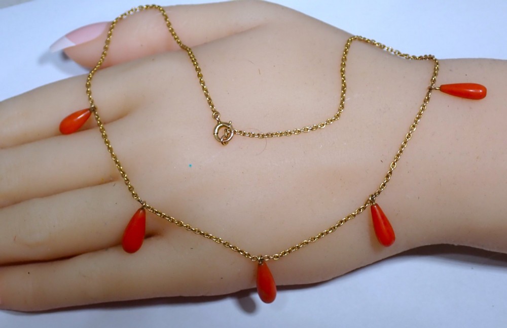 A slender gold link chain necklace featuring five suspended teardrop-shaped red coral drops and a bolt ring clasp.