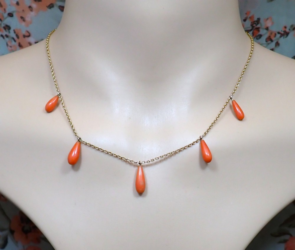 A slender gold link chain necklace featuring five suspended teardrop-shaped red coral drops and a bolt ring clasp. View III
