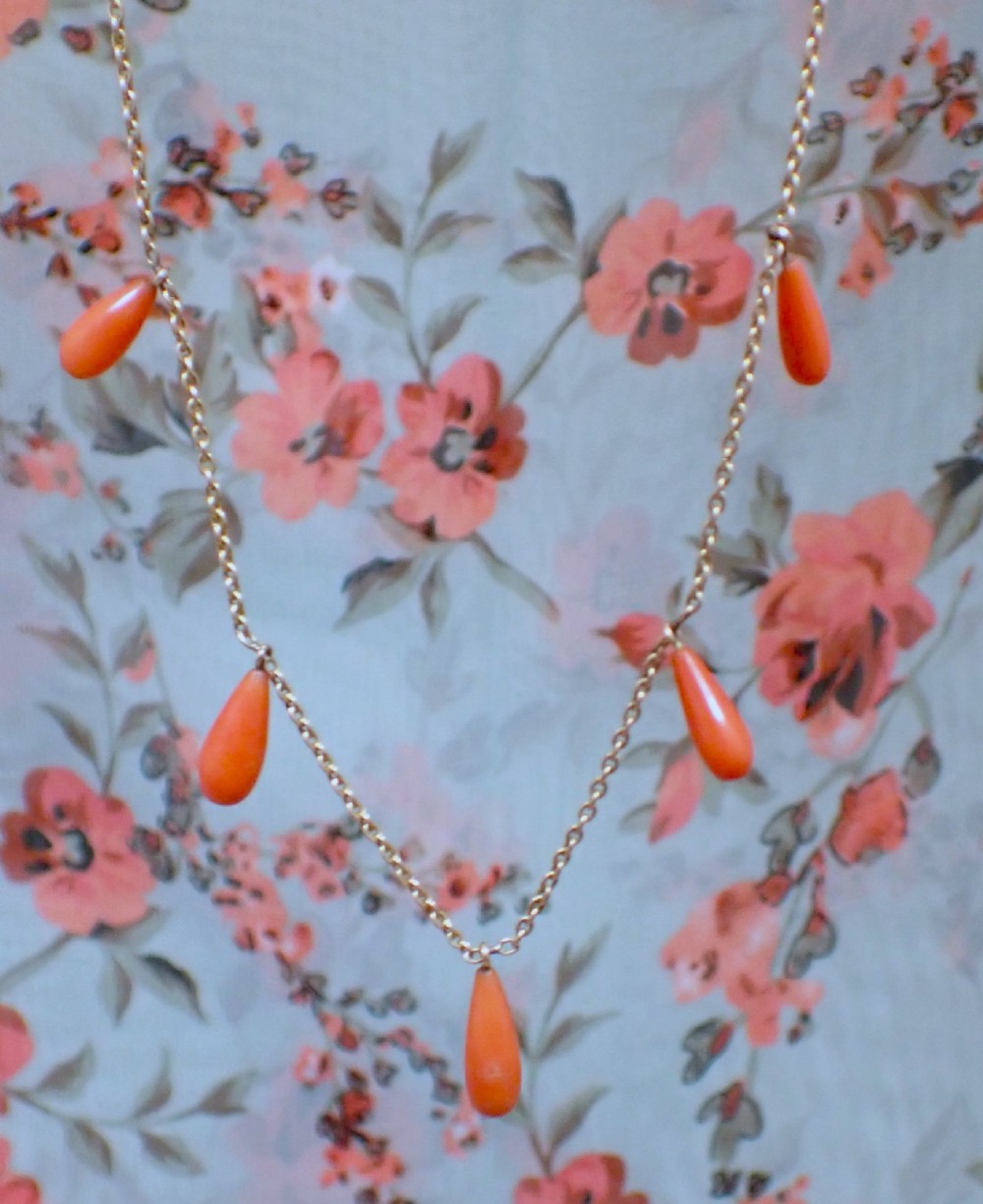 A slender gold link chain necklace featuring five suspended teardrop-shaped red coral drops and a bolt ring clasp. View II