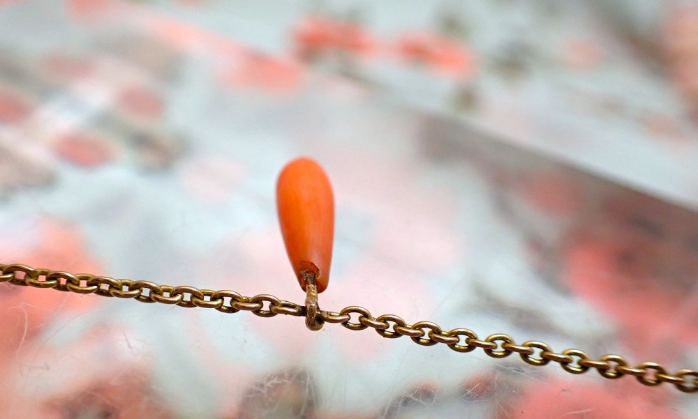 A slender gold link chain necklace featuring five suspended teardrop-shaped red coral drops and a bolt ring clasp. View IV