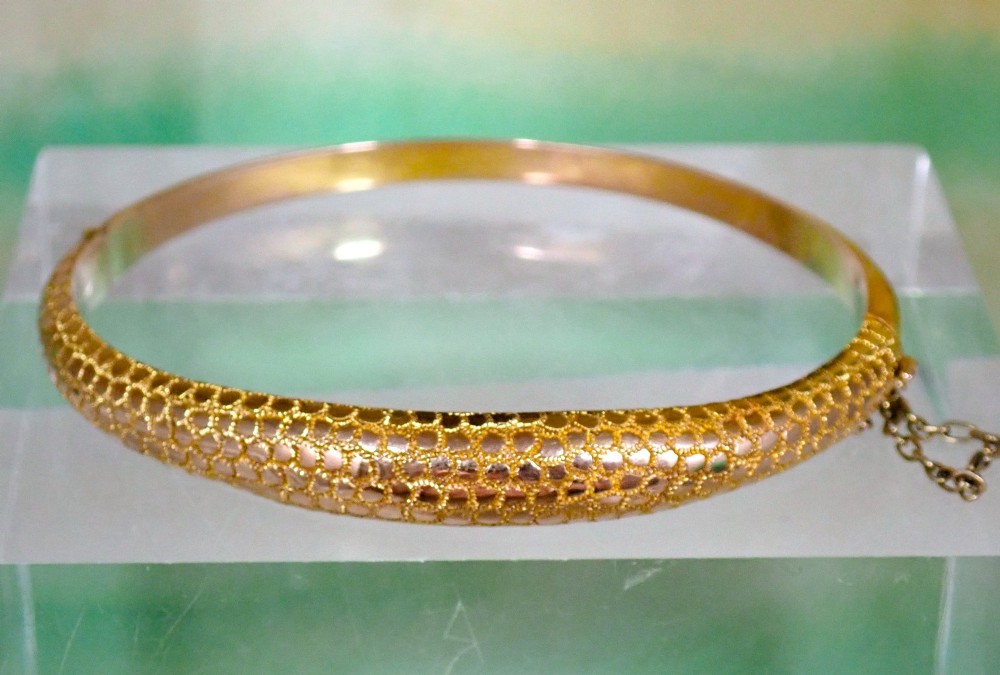 An antique Victorian hinged gold bangle featuring a textured honeycomb pattern across the upper band with a side safety chain.