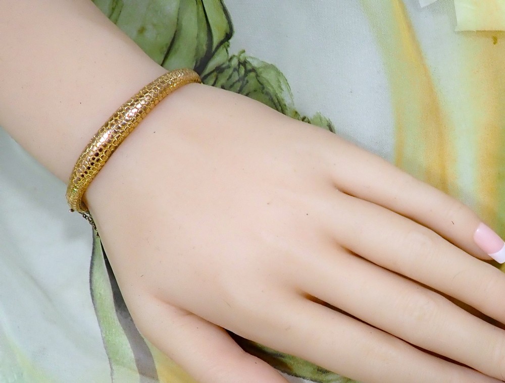 An antique Victorian hinged gold bangle featuring a textured honeycomb pattern across the upper band with a side safety chain. View II