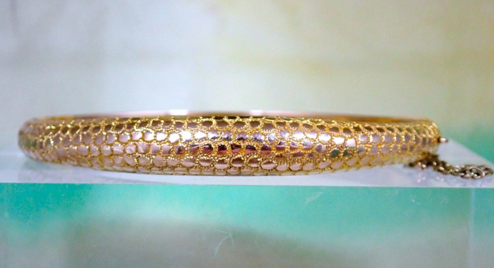 An antique Victorian hinged gold bangle featuring a textured honeycomb pattern across the upper band with a side safety chain. View III