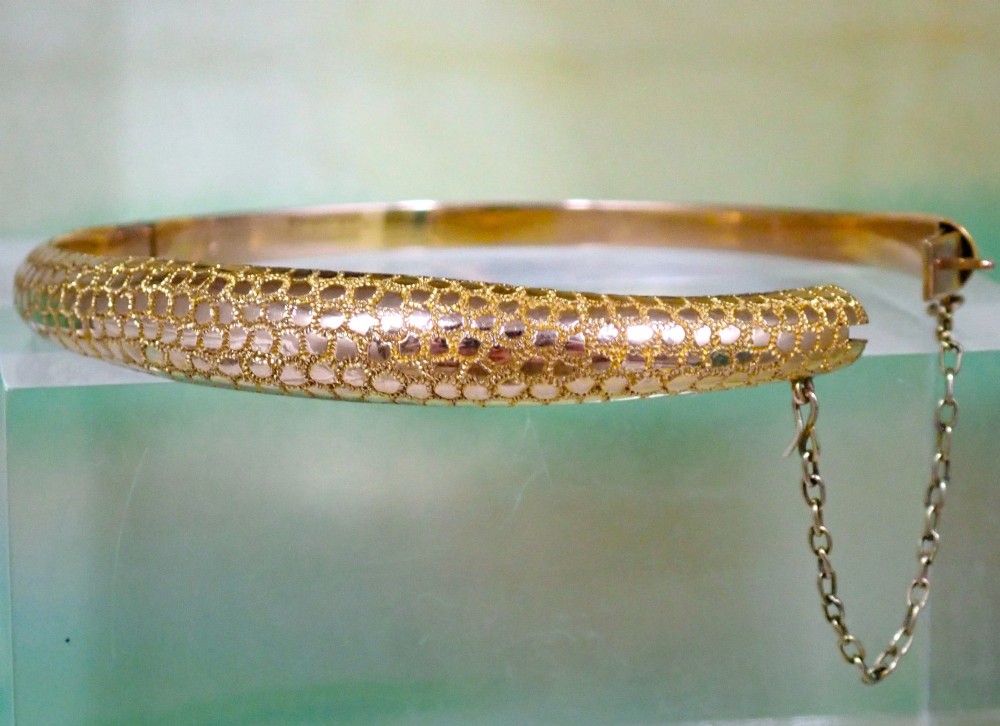 An antique Victorian hinged gold bangle featuring a textured honeycomb pattern across the upper band with a side safety chain. View IV