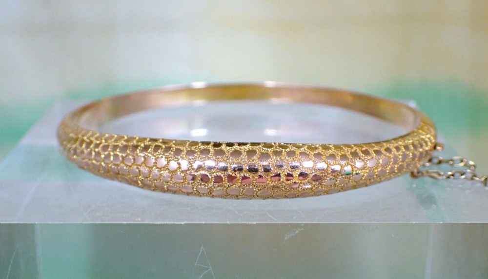 An antique Victorian hinged gold bangle featuring a textured honeycomb pattern across the upper band with a side safety chain. View VII