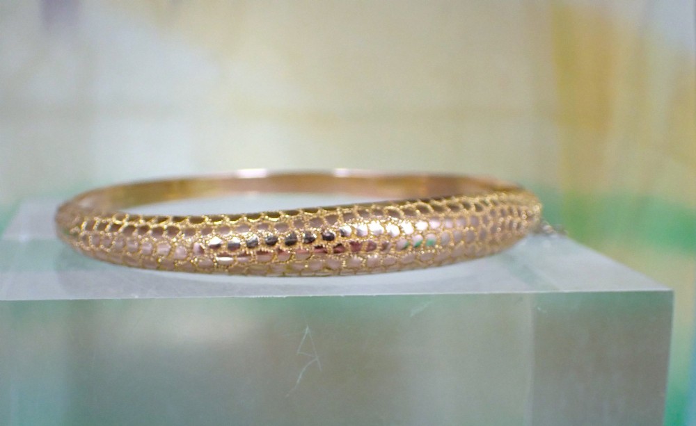 An antique Victorian hinged gold bangle featuring a textured honeycomb pattern across the upper band with a side safety chain. View VIII