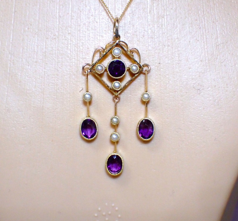 An Art Nouveau 15ct yellow gold openwork diamond-shaped pendant featuring a central round amethyst, seed pearls, and three dangling purple amethyst drops.