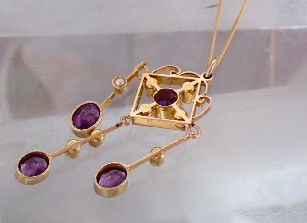 An Art Nouveau 15ct yellow gold openwork diamond-shaped pendant featuring a central round amethyst, seed pearls, and three dangling purple amethyst drops. View IV