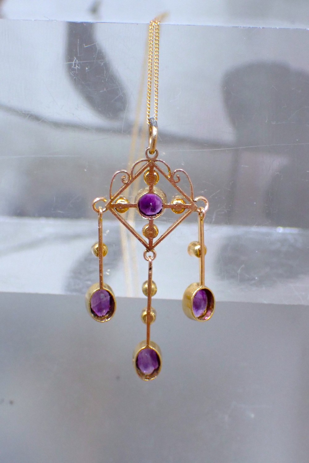 An Art Nouveau 15ct yellow gold openwork diamond-shaped pendant featuring a central round amethyst, seed pearls, and three dangling purple amethyst drops. View V