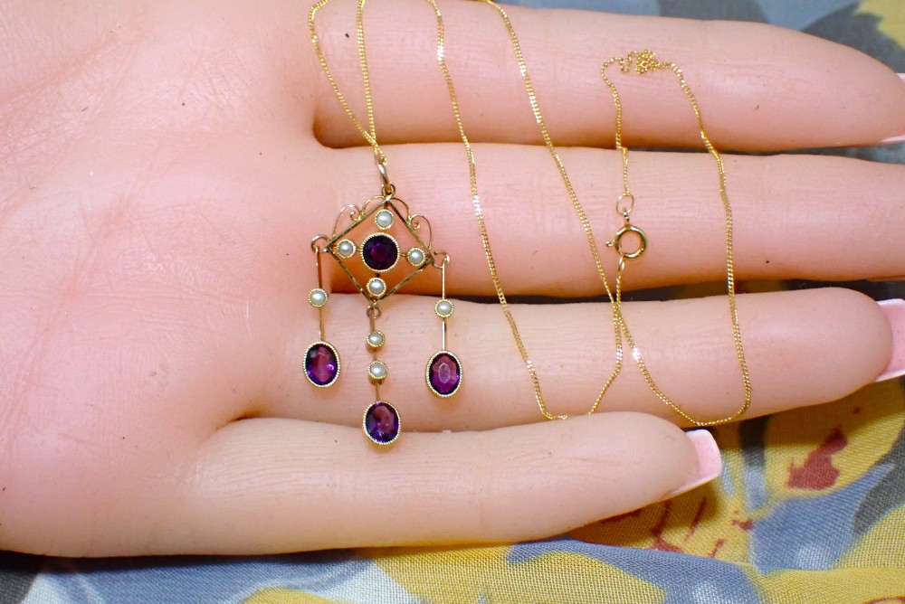 An Art Nouveau 15ct yellow gold openwork diamond-shaped pendant featuring a central round amethyst, seed pearls, and three dangling purple amethyst drops. View VI