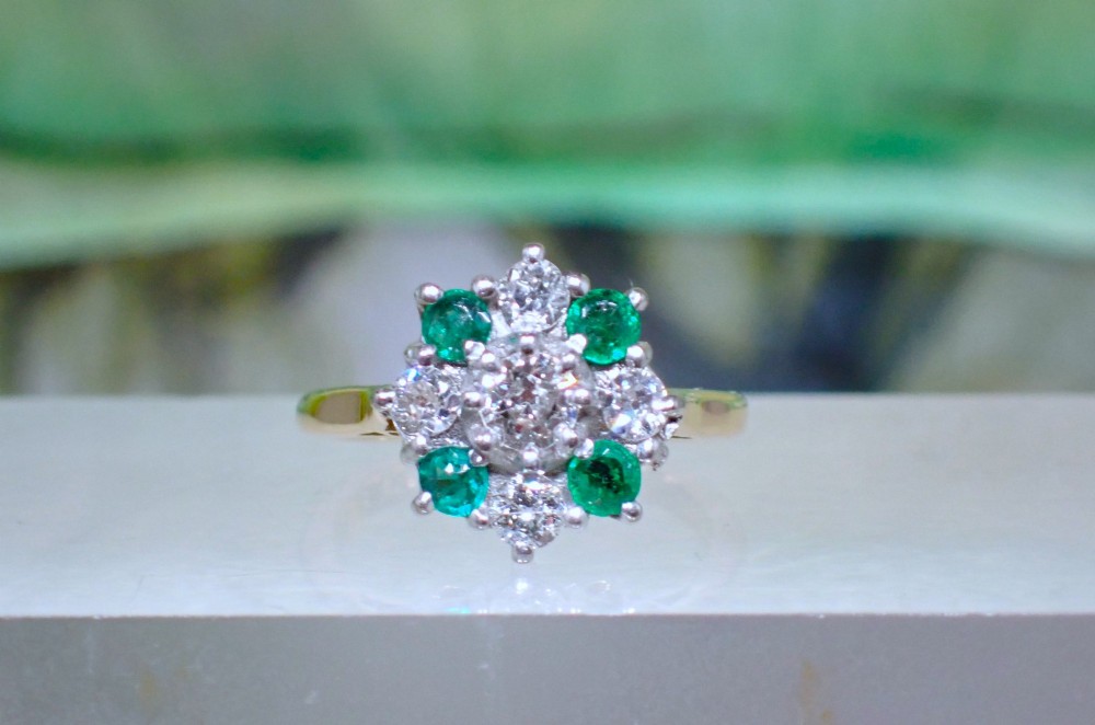 A Mid-century 18ct yellow gold cluster ring set with a central round diamond surrounded by alternating emeralds and diamonds.