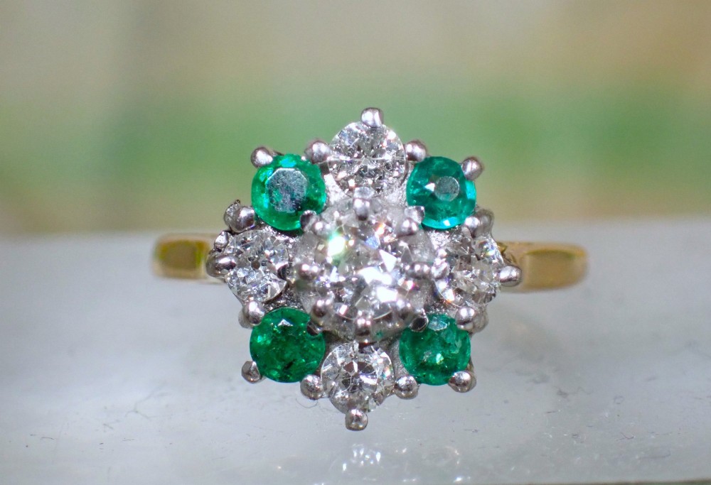 A Mid-century 18ct yellow gold cluster ring set with a central round diamond surrounded by alternating emeralds and diamonds. View II