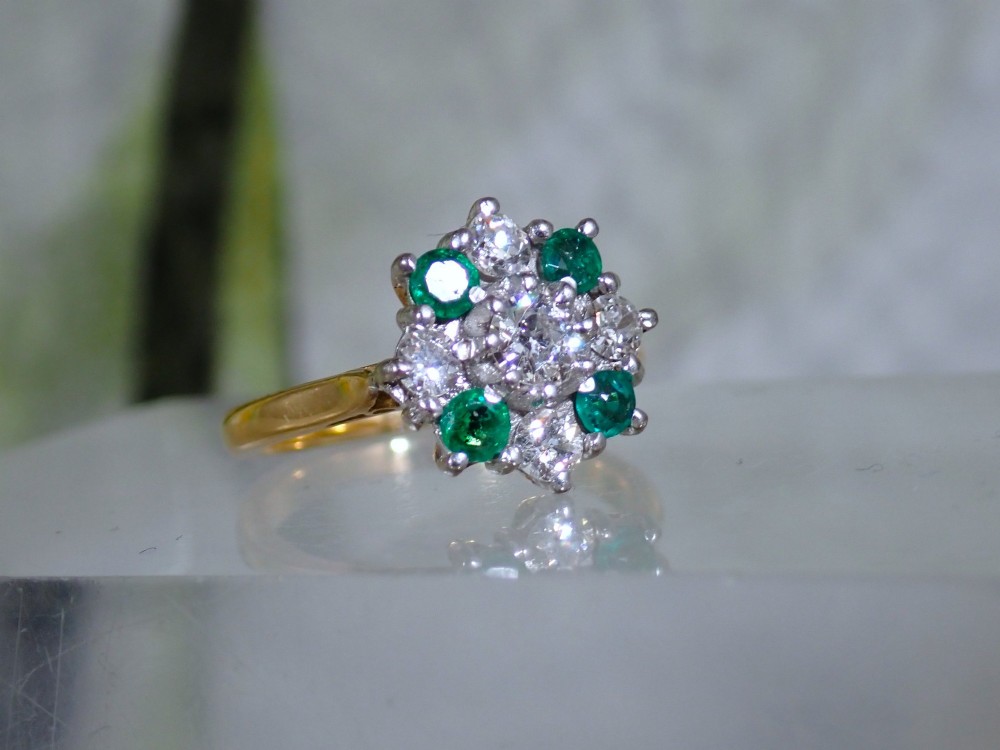 A Mid-century 18ct yellow gold cluster ring set with a central round diamond surrounded by alternating emeralds and diamonds. View IV
