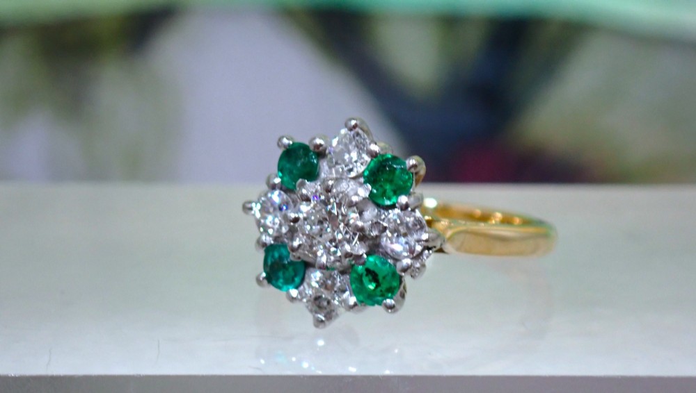 A Mid-century 18ct yellow gold cluster ring set with a central round diamond surrounded by alternating emeralds and diamonds. View V