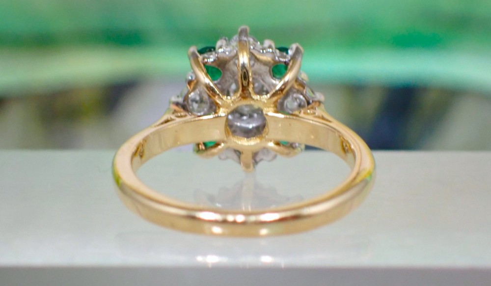 A Mid-century 18ct yellow gold cluster ring set with a central round diamond surrounded by alternating emeralds and diamonds. View VI